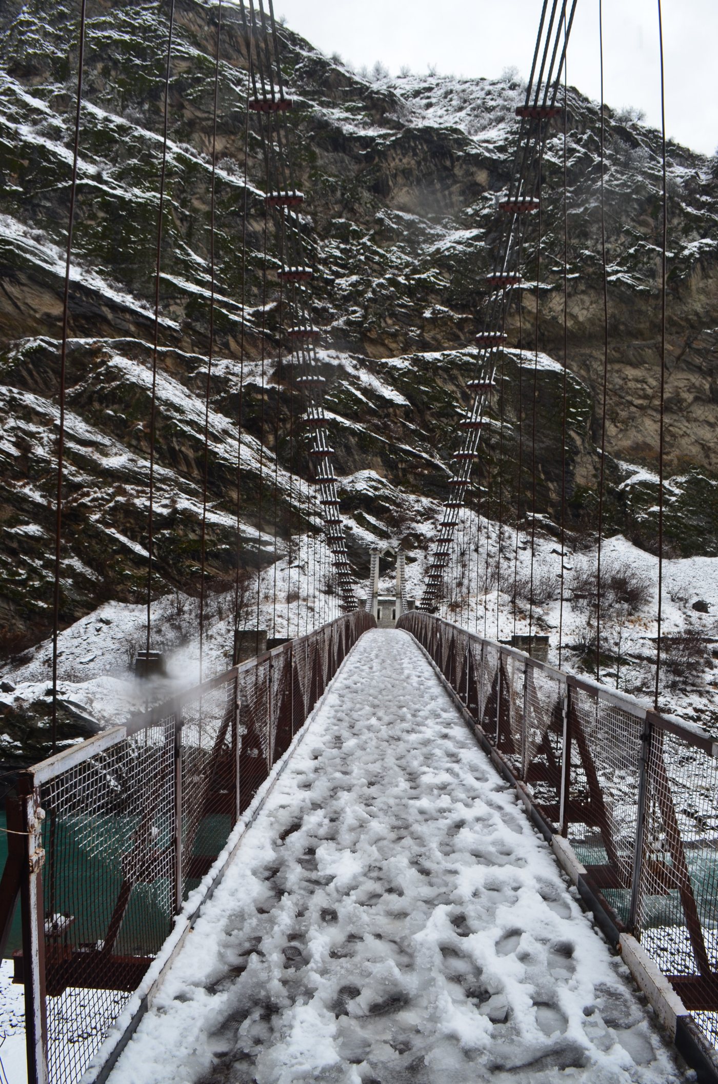 Snow-covered suspension bridge in Pangi Valley